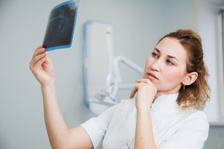 Female doctor dentist examining x-ray of human jaw. Professional stomatologist checking dental x-ray image at clinic office.の写真素材