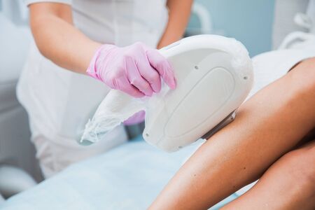 Laser hair removal, photoepilation, body and skin care concept. Young woman remove hair on legs at cosmetology clinic.の写真素材