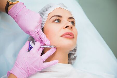 Young woman at cosmetologist office remove wrinkles on face contour. Toxin injections, anti-age procedure, skincare concept. Doctor and patient.の写真素材