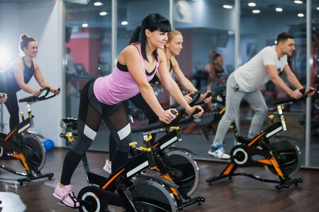 Cycling class in fitness club, group of fit people spinning on cardio machine. Man and women do sports exercises at gym fat burning class. Active lifestyle, health care and body training conceptの写真素材