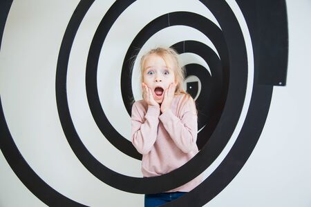 Surprised little girl with emotional face into black spiral at studio. Shocked, horrified child, unexpected scene. Human reaction concept.の写真素材