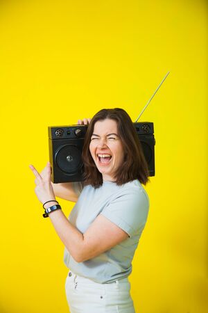 Happy young woman with retro music player. Nostalgic emotional female model. Old tape recorder, female expressive person.の写真素材