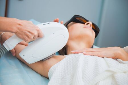 Laser hair removal, photoepilation, body and skin care concept. Young woman remove hair on armpits at cosmetology clinic. Closeup shot, unrecognizable female people.の写真素材