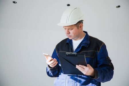 Builder foreman in a white helmet at a construction site indoors, architect flat renovation, professional foreman at work discussing by smartphoneの写真素材