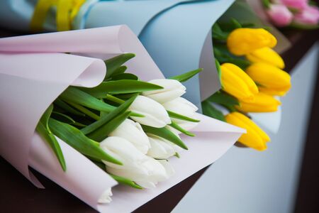 Beautiful tulips in craft paper lie on table ready for delivery on women's day march 8. A bright background of spring flower blossoms. Floristics and holiday preparation. Floral design conceptの写真素材