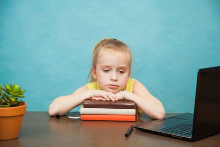 Little sad school girl study at home with laptop and books. First grade female pupil learn lessons by internet online. Social distance during quarantine, self-isolation, online education conceptの写真素材