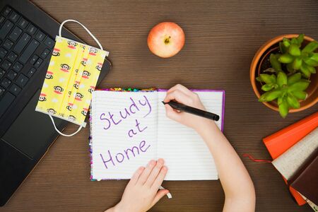 Lay flat image child hands medical antiviral mask write in paper notebook study at home. Little elementary student ready for online lessons. Social distance, quarantine isolation concept.の写真素材