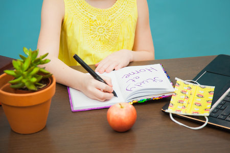 Closeup image child hands medical antiviral mask write in paper notebook study at home. Little...