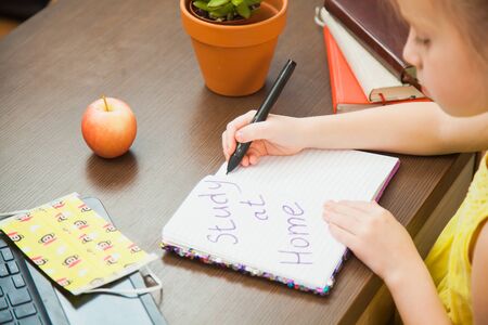 Closeup image child hands medical antiviral mask write in paper notebook study at home. Little elementary student ready for online lessons. Social distance, quarantine isolation concept.の写真素材