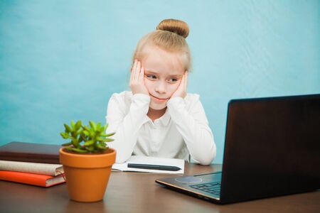 Little sad school girl study at home with laptop and books. First grade female pupil learn lessons by internet online. Social distance during quarantine, self-isolation, online education conceptの写真素材