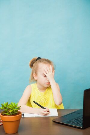 Little sad school girl study at home with laptop and books. First grade female pupil learn lessons by internet online. Social distance during quarantine, self-isolation, online education conceptの写真素材