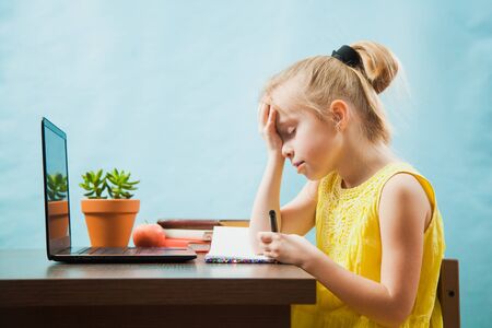 Little sad school girl study at home with laptop and books. First grade female pupil learn lessons by internet online. Social distance during quarantine, self-isolation, online education conceptの写真素材
