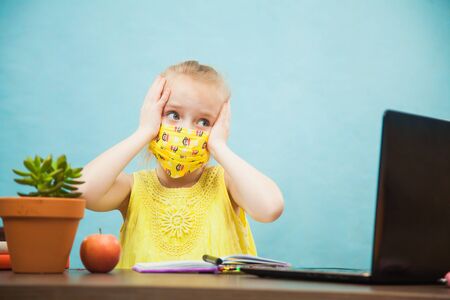 Little school girl in panic study at home with laptop and antiviral mask. First grade pupil learn lessons by internet online. Social distance on quarantine, self-isolation, online education conceptの写真素材