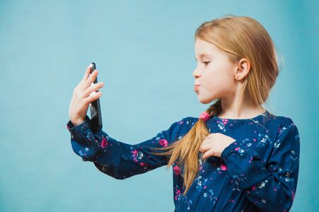 Preteen girl making selfie on smartphone. Little child model with modern phone photoshooting herself. Trend, young generation, social media, gadget concept.の写真素材