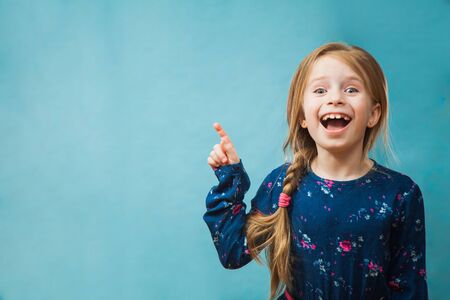 Pretty little girl poits to the left, copy space for some text. Smiling female child, preteen girl in blue dress shows something. Advertising concept.の写真素材