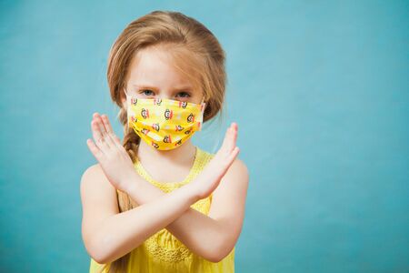 Cute blond preteen girl in antiviral medical mask shows stop gesture. Pretty female child says no to virus, people against pandemic, copy space foe text, advertising concept.の写真素材