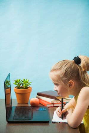 Happy elementary student girl homeschooling on laptop online by internet. First grade female pupil learn lessons by computer. Social distance during quarantine, self-isolation conceptの写真素材