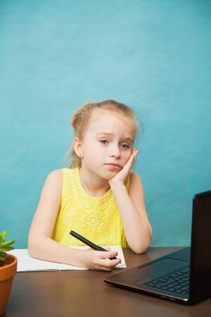 Sad tired elementary student girl homeschooling on laptop online by internet. First grade female pupil learn lessons by computer. Social distance during quarantine, self-isolation conceptの写真素材