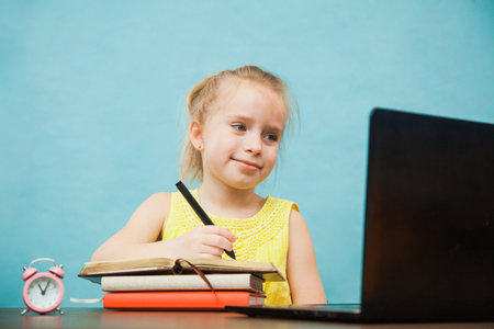 Happy elementary student girl homeschooling on laptop online by internet. First grade female pupil...