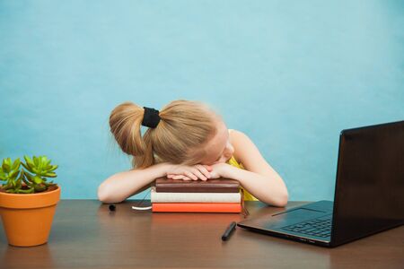 Little primary school girl in antiviral mask sleep on table near laptop on home isolation. Tired of online education child got asleep, social distance during quarantine, self-isolation conceptの写真素材