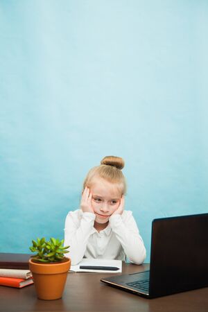 Sad tired elementary student girl homeschooling on laptop online by internet. First grade female pupil learn lessons by computer. Social distance during quarantine, self-isolation conceptの写真素材