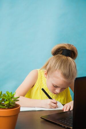 Hardworking elementary student girl homeschooling on laptop online by internet. First grade female pupil learn lessons by computer. Social distance during quarantine, self-isolation conceptの写真素材