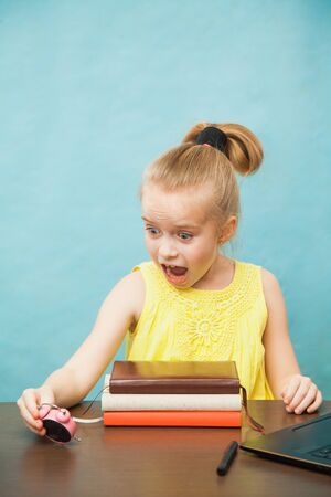 Little elementary age girl homeschooling with books, laptop and alarm clock. Over worked pupil do lessons at home. Time management on qaurantine, self-isolation and social distancing concept.の写真素材