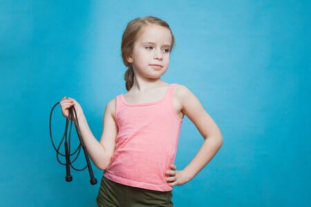 Pretty little sporty girl with skipping rope on blue background. Preteen child doing gymnastics, fitness and active games. Healthy lifestyle from early age.の写真素材