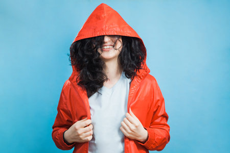 Happy pretty young girl in red coat hood with dark curly hair and open smile. Portrait of smiling...