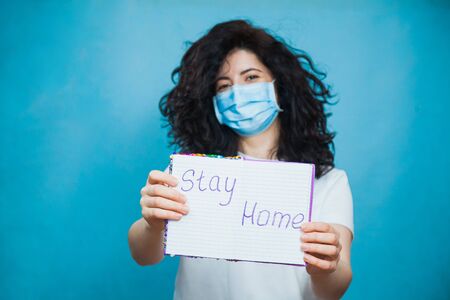 Young and beautiful woman in antiviral mask holding written text stay home. Social distance, quarantine isolation, virus prevention concept.の写真素材