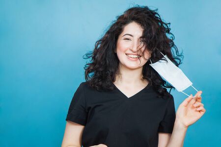 Beautiful happy black haired woman taking off medical antiviral mask. Young female person remove protective, end of viral outbreak, quarantine and social distancing concept.の写真素材