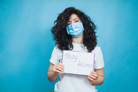 Young and beautiful woman in antiviral mask holding written text stay home. Social distance, quarantine isolation, virus prevention concept.の写真素材