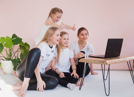 Four young sisters smile and look at monitor of laptop. Family use internet chat on quarantine, social life online, home isolation concept.の写真素材