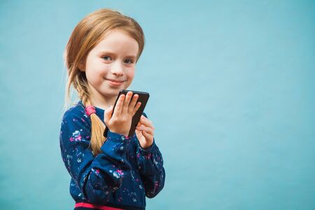 Happy preteen girl using smartphone, texting message. Female gen z person using gadgeton blue background, copy space fot text.の写真素材