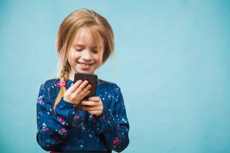 Happy preteen girl using smartphone, texting message. Female gen z person using gadgeton blue background, copy space fot text.の写真素材
