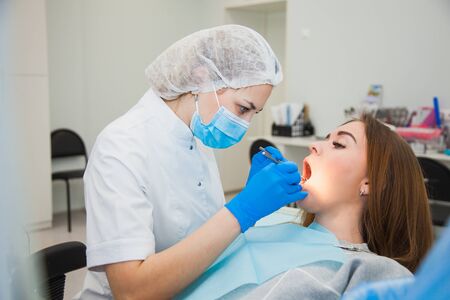 Young female dentist curing patients teeth filling cavity. Stomatologist working with professional equipment in clinic office.の写真素材