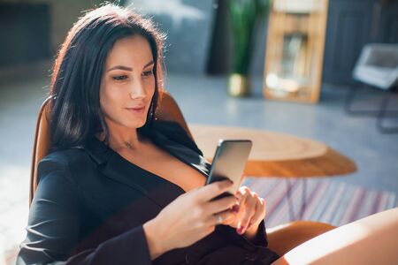 Beautiful sexy blogger using smartphone at home. Young business lady with mobile phone texting message, working from home.の写真素材