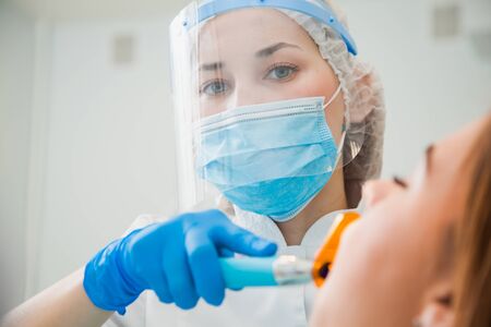 Young female dentist curing patients teeth filling cavity. Stomatologist working with professional equipment in clinic office.の写真素材