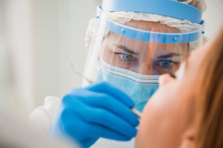 Young female dentist curing patient's teeth filling cavity. Stomatologist working with professional equipment in clinic office. Close-up shot, teeth care and medicine conceptの写真素材