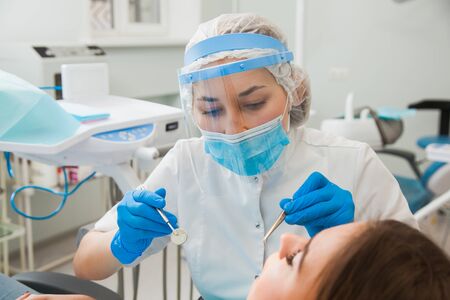 Young female dentist curing patients teeth filling cavity. Stomatologist working with professional equipment in clinic office.の写真素材