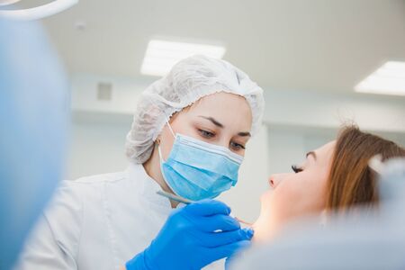 Young female dentist curing patients teeth filling cavity. Stomatologist working with professional equipment in clinic office. Close-up shot, teeth care and medicine conceptの写真素材