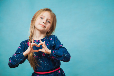 Happy delighted girl in casual classic blue dress smile with hands in heart shape. Positive emotion,...