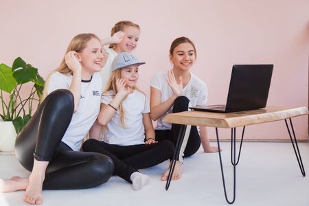 Four young sisters smile and look at monitor of laptop. Family use internet chat on quarantine, social life online, home isolation concept.の写真素材