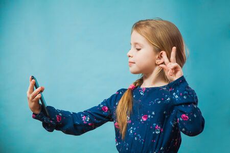 Preteen girl making selfie on smartphone. Little child model with modern phone photoshooting herself. Trend, young generation, social media, gadget concept. Copy spaceの写真素材