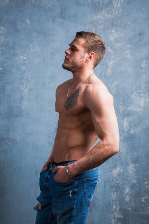 Vertical shot of muscular man with naked torso. Fitness model in denim on grey background.の写真素材