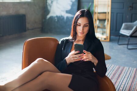 Beautiful sexy blogger using smartphone at home. Young business lady with mobile phone texting message, working from home.の写真素材