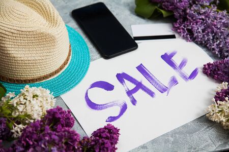 Handwritten word sale in white frame, smartphone, credit card lay in lilac blossom. Shopping concept.の写真素材