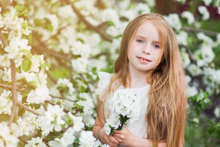 Beautiful preteen girl with long blond hair enjoy spring apple blooming. Little preschool girl in garden tree flowers. Copy space for text.の写真素材