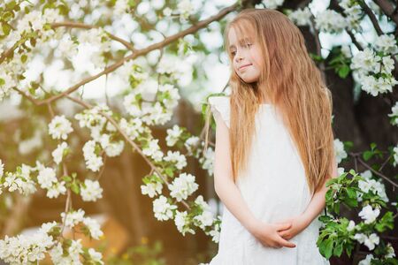 Beautiful preteen girl with long blond hair enjoy spring apple blooming. Little preschool girl in garden tree flowers. Copy space for text.の写真素材