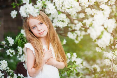 Beautiful preteen girl with long blond hair enjoy spring apple blooming. Little preschool girl in garden tree flowers. Copy space for text.の写真素材